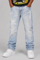 A person wearing light-wash, heavily distressed and relaxed straight blue jeans with ruched details, paired with white sneakers and a black graphic t-shirt, shown from the waist down on a neutral gray background. By Fresh N Fitted.