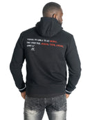 A man viewed from behind wearing a black hoodie with white and red text printed on the back, featuring decorative studs along the shoulders and cuffs. He is also wearing gray jeans against a plain white background.