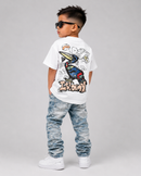 A young boy wearing a white graphic t-shirt, light-wash distressed jeans, and white sneakers, photographed from the back against a neutral gray studio background.