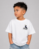 A young boy wearing a white short-sleeve t-shirt with a small black and blue graphic on the left chest, paired with light blue jeans, photographed against a solid gray background.