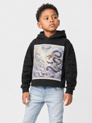 A young boy wearing a black cropped hoodie with a large graphic print of a blue and gold dragon on the front, paired with light blue jeans, photographed against a light gray studio background.