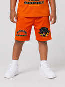 A child wearing bright orange mesh basketball shorts with 'POWER RESPECT' text and a black dog graphic on the left leg, paired with a matching orange shirt and white sneakers, shown against a light gray studio background.