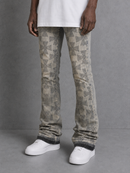A person wearing patterned beige and gray flared jeans with a geometric print, styled with a white t-shirt and white sneakers against a gray studio background.