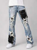 Light-wash blue denim jeans with distressed rips and large black-and-white patchwork embellishments on the thighs and lower legs, shown on a model from the waist down against a light gray studio background.