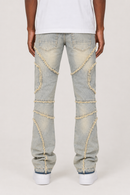 A person shown from the back wearing light-wash distressed jeans with decorative frayed patchwork details running down the legs, paired with a white t-shirt and white sneakers on a light gray studio background.