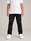A child wearing black distressed jeans with ripped details, a plain white t-shirt, and white sneakers, standing against a neutral light gray studio background.