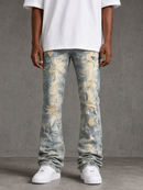 A person wearing distressed light blue denim jeans with a faded yellow/gold acid-wash effect, paired with a white t-shirt and white sneakers, standing against a textured gray studio background.