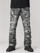 Distressed gray and black acid-wash jeans with ripped details, shown on a model from the waist down wearing black sneakers against a light gray studio background.