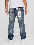 Rear view of a person wearing distressed blue jeans with white sneakers and a white t-shirt, showing the back pockets and patches of the jeans against a light gray studio background.