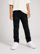 A child wearing distressed black skinny jeans with faded detailing, styled with an off-white t-shirt and white sneakers against a light gray studio background.