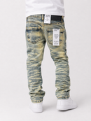 Rear view of a person wearing slim-fit jeans with a yellow-green and blue acid-wash/distressed pattern, paired with a white t-shirt and white sneakers, on a light gray studio background.