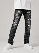 A person wearing distressed black acid-wash jeans with ripped details, paired with a white t-shirt and white sneakers, shown from the waist down on a light gray studio background.