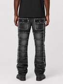 Rear view of a person wearing dark distressed denim jeans with horizontal frayed panel details and large back pockets, paired with a black top and black shoes on a light gray studio background.
