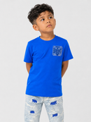 A young boy wearing a bright blue short-sleeve t-shirt with a light blue geometric graphic on the left chest, paired with light-wash distressed jeans, photographed against a solid light gray background.