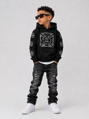 A young boy modeling a black hoodie with a gray graphic print, distressed black jeans, and white sneakers, standing against a light gray studio background.