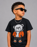 A child wearing a black short-sleeve graphic T-shirt with a large teddy bear design in white, gray, and orange, styled with black sunglasses and a silver chain against a plain gray background.