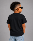 A child model shown from the back wearing a black short-sleeve crewneck t-shirt, light blue jeans, and black sunglasses against a solid gray studio background.