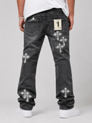 Rear view of a person wearing washed black denim jeans with multiple silver cross patches and a white t-shirt, shown against a light gray studio background.