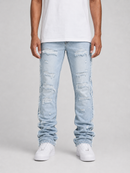 A person wearing light-wash distressed denim jeans with ripped details and side frayed edges, paired with a white t-shirt and white sneakers, shown from the waist down on a light gray studio background.