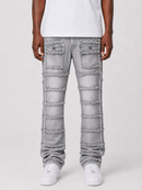 A person wearing light gray distressed denim jeans with horizontal frayed panel details and flap pockets, paired with a white t-shirt and white sneakers against a light gray studio background.