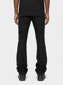 Rear view of a person wearing black jeans and black shoes against a light gray studio background.