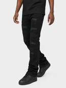 A person wearing black distressed jeans with ripped details, paired with a black t-shirt and black sneakers, shown from the waist down against a light gray studio background.