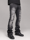 Distressed black denim jeans with heavy fading and ripped details, shown on a model from the waist down wearing black shoes against a gray studio background.