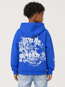 A child shown from the back wearing a bright blue hoodie with a large white graphic print on the back, paired with light blue jeans, against a light gray studio background.