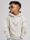 A young boy wearing a light beige Givenchy hoodie with black graphic prints on the sleeves and chest, styled with white-framed sunglasses, against a solid light gray background.