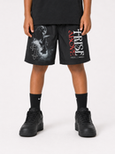 A person wearing black shorts with a large graphic print featuring a skull, a cross, and the text 'CHRIST ABOVE' in white and red, styled with black crew socks and black sneakers against a light gray studio background.