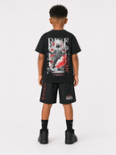 A child model viewed from the back wearing a black graphic t-shirt and matching black shorts with red and white print details, styled with black socks and sneakers against a light gray studio background.