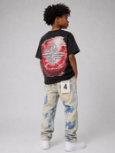 A child model shown from the back wearing a black t-shirt with a large red and silver graphic print, paired with distressed light blue and beige jeans featuring a white paper tag with the number 4, and white sneakers, against a neutral gray studio background. By Fresh N Fitted