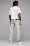 A man viewed from behind wearing light-wash gray jeans, a white t-shirt, and white sneakers against a solid gray studio background. By Fresh N Fitted