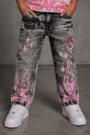 A person wearing acid-washed black denim jeans with pink flame and star graphics, paired with white sneakers, shown from the waist down against a gray studio background. by Fresh N Fitted