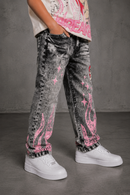 A person wearing acid-wash black jeans with pink flame and star graphics, paired with white sneakers and a graphic t-shirt, standing against a gray concrete wall. By Fresh N Fitted.