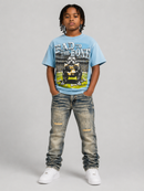 A child model wearing a light blue graphic t-shirt with a bulldog print and the text 'HAD TO THE BONE', paired with distressed gray jeans and white sneakers, standing against a neutral gray studio background. By Fresh N Fitted.