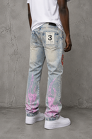 A person shown from the back wearing light-tint jeans with pink flame-like down both legs, a white t-shirt, and white sneakers, standing against a textured gray concrete wall. By Fresh N Fitted.