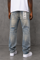 A person shown from the back wearing light-tint distressed jeans with a white t-shirt and white sneakers, standing against a textured gray wall. By Fresh N Fitted.