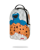 A Sprayground backpack featuring a graphic print of the Cookie Monster peeking out from a giant chocolate chip cookie, set against a clean white background with a soft drop shadow.