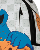Close-up of a backpack featuring a Cookie Monster graphic print with blue hair, an orange shirt, and a white patterned background, showing black zippers and a vertical zip pocket.