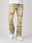 Distressed light-wash denim jeans with heavy rips and frayed edges, shown on a model from the waist down wearing white sneakers against a light gray studio background.