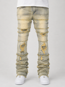 Distressed light-wash denim jeans with heavy fraying, rips, and faded yellowing, shown on a model from the waist down wearing white sneakers against a light gray background.