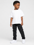 A young boy modeling a white short-sleeve crewneck t-shirt, black cargo pants, and white sneakers, standing against a light gray studio background.