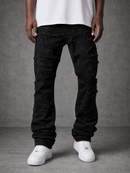 A person wearing distressed black jeans with frayed and ripped detailing, paired with a white t-shirt and white sneakers, standing against a textured gray studio background.