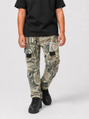 A person wearing camouflage cargo pants with a black t-shirt and black sneakers, shown from the chest down against a light gray studio background.