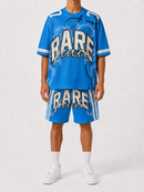 A model wearing a blue athletic t-shirt and matching shorts set from Rare Prince, featuring a white and black graphic print on the front and white stripes down the sides, paired with white socks and sneakers against a light gray studio background.