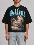 Black Silent Verse Raised By An Angel oversized cropped T-shirt displayed on a hanger with a relaxed fit and bold graphic print.