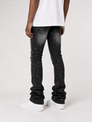 A person shown from the back wearing black jeans with a white speckled galaxy print, a white t-shirt, and white sneakers against a light gray studio background.