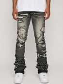 Distressed black wash skinny jeans with heavy ripped detailing and ruffled hems, shown on a model wearing a white t-shirt and white sneakers against a light gray background.