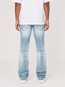 A person shown from the back wearing light-wash blue jeans with a faded wash and a white t-shirt, standing against a light gray studio background.